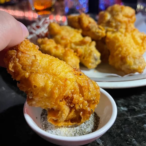 Hand dipping a crispy fried Korean chicken wing into a small bowl of seasoning.