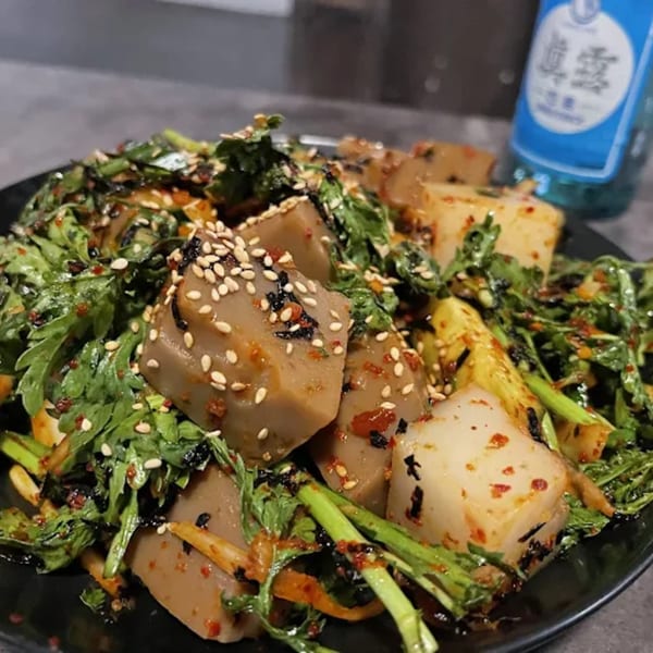 Korean acorn jelly salad with green vegetables, sesame seeds, and a blue bottle in the background.