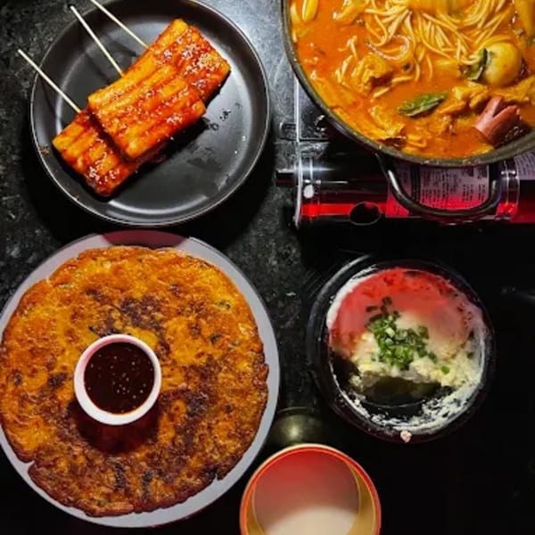 Overhead view of Korean dishes: tteokbokki skewers, kimchi pancake, budae jjigae, and steamed egg.