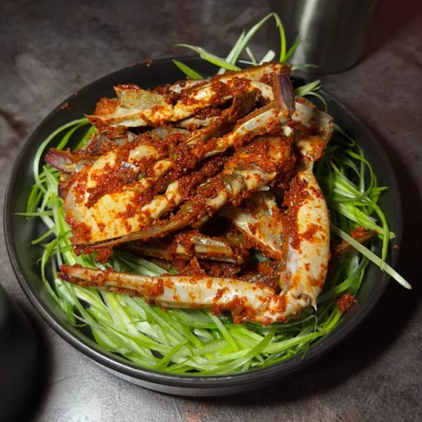 Spicy Korean marinated raw crab (Ganjang Gejang) on a bed of green onions in a dark bowl.