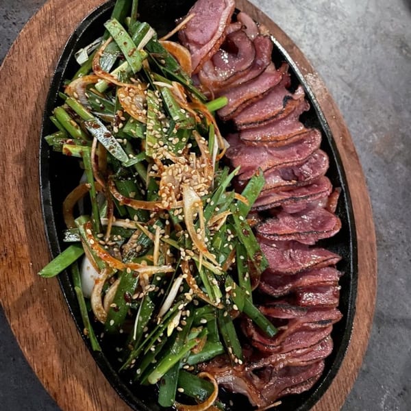 Sizzling Korean duck slices with green onions and sesame seeds on a black platter.